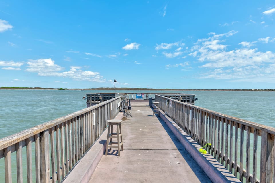 Private fishing pier extends into crystal-clear waters under endless blue skies, perfect for casting a line or watching sunset.