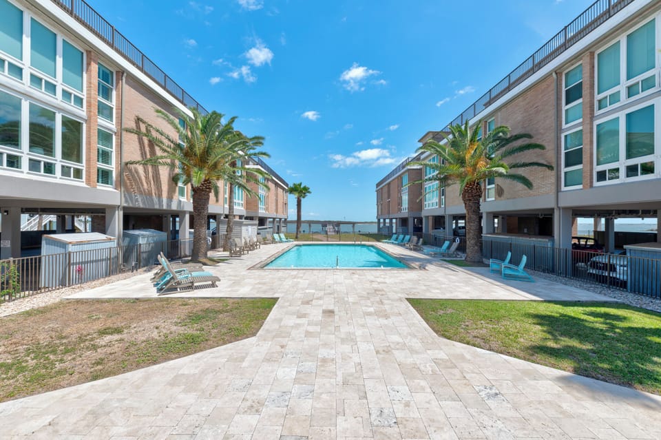 Modern beachfront resort complex with swimming pool surrounded by contemporary buildings and tropical palm trees.
