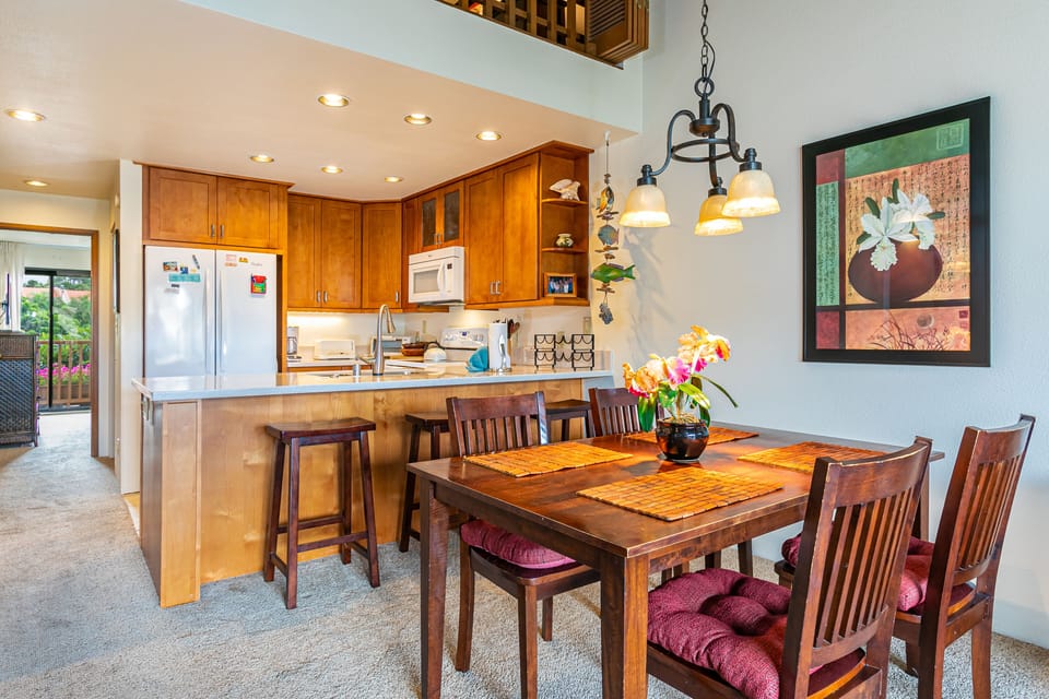 Gather around the warm wood dining table under ambient lighting, with a fully-equipped kitchen at your fingertips featuring rich cabinetry, modern appliances, and a breakfast bar for casual mornings together.