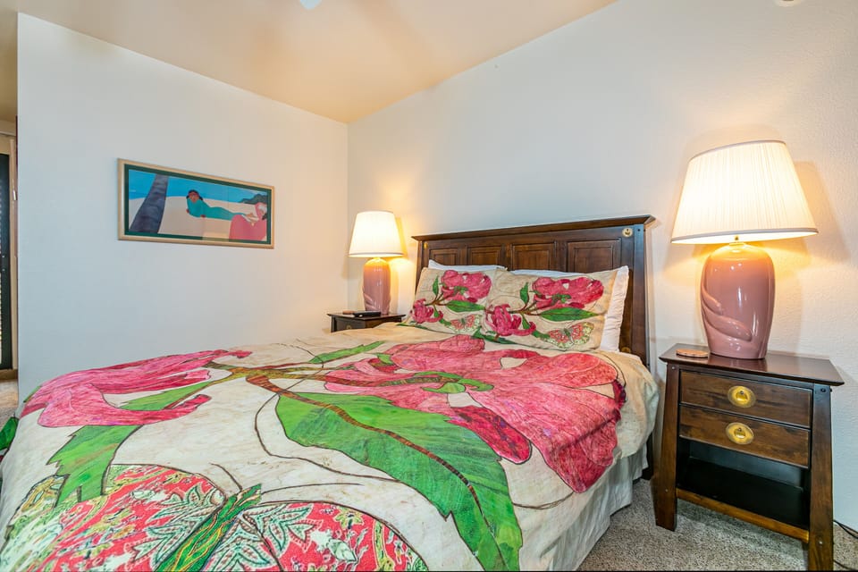 Sink into your plush bed adorned with vibrant floral linens, flanked by warm pink lamps that cast a cozy glow—your peaceful retreat awaits.