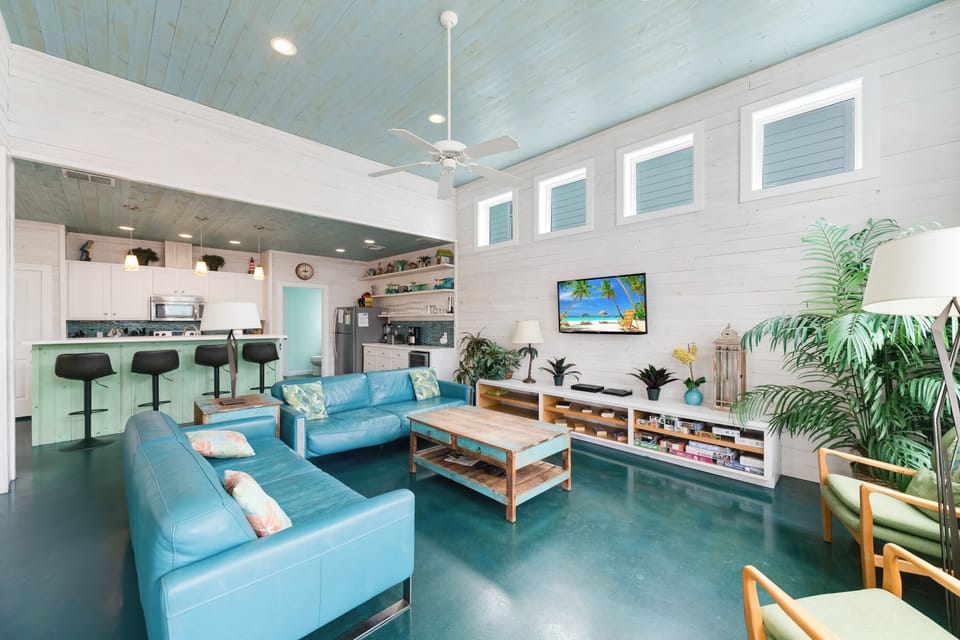 Relax in your open-concept living space with coastal blue accents, modern kitchen, and tropical vibes that make every moment feel like vacation.