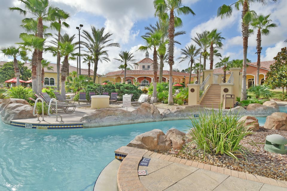 A tropical pool area with palm trees, rocks, and lounge chairs.