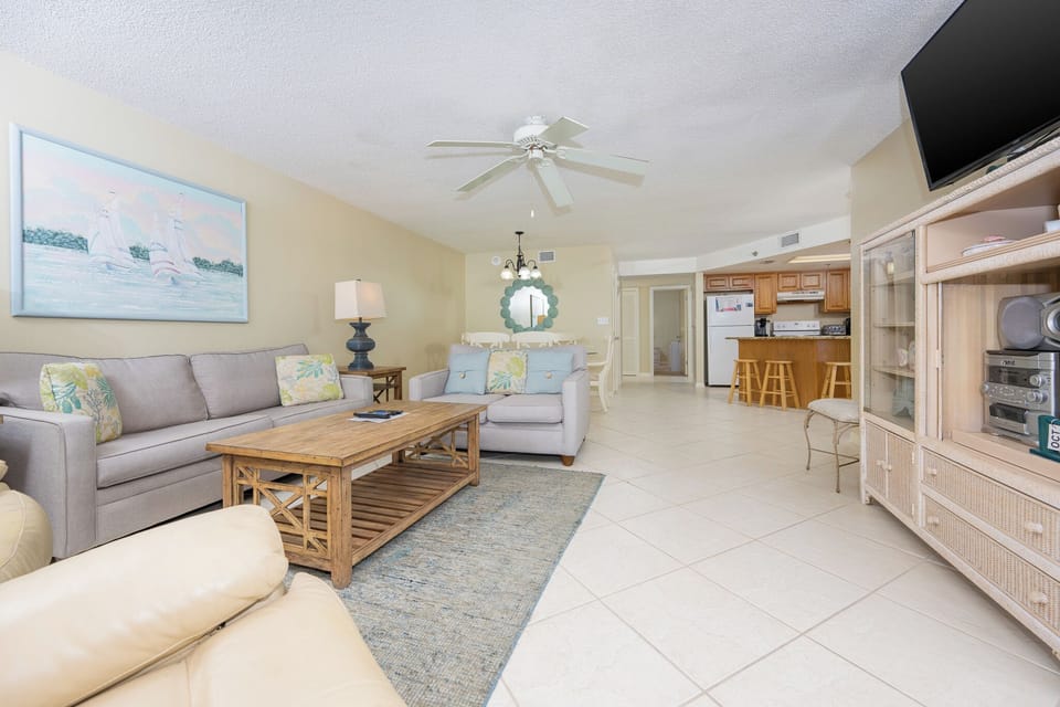 The inviting living area features a light gray sofa with floral accents, a rustic coffee table, and view into the kitchen