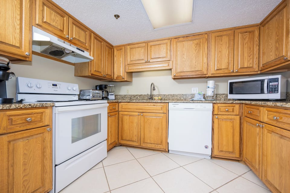 Bright kitchen featuring wooden cabinetry, granite countertops, and a full suite of appliances for convenient meal prep