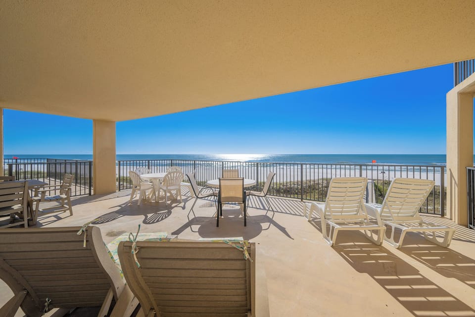 The spacious extended balcony features lounge chairs and a dining table, offering a direct view of the beach and gulf water