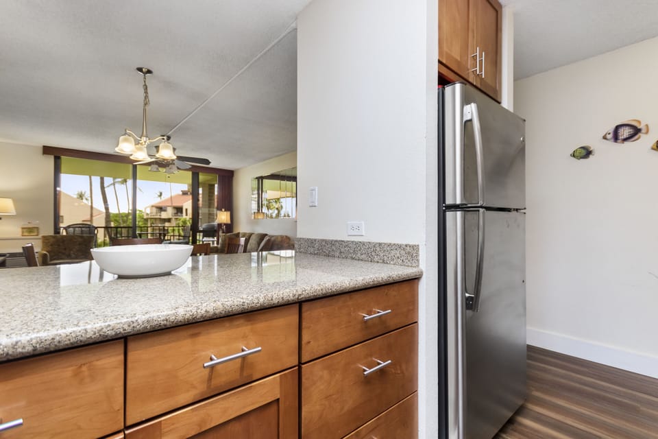 Your island kitchen features sleek granite counters and stainless appliances, opening seamlessly to the bright living space with tropical views that welcome you home.