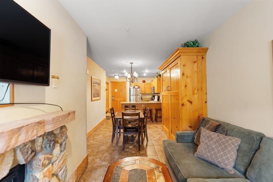 Relax in your cozy living space with warm wood accents, stone fireplace, and fully equipped kitchen—perfect for unwinding after mountain adventures.