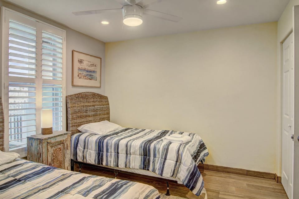 Drift off in your coastal-inspired bedroom featuring twin beds with nautical linens and wicker headboards beneath gentle ceiling fan breezes.