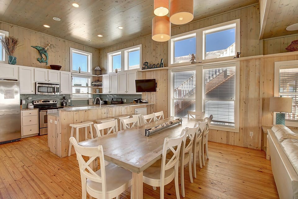 You'll love gathering in this warm, beachy kitchen with rustic wood walls, spacious dining table, and modern appliances perfect for cooking together.