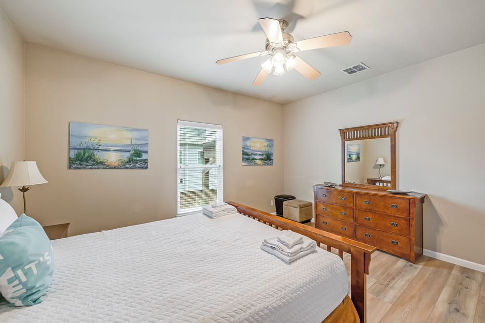 Relax in your peaceful bedroom with coastal artwork, comfortable bedding, and natural light streaming through your window.