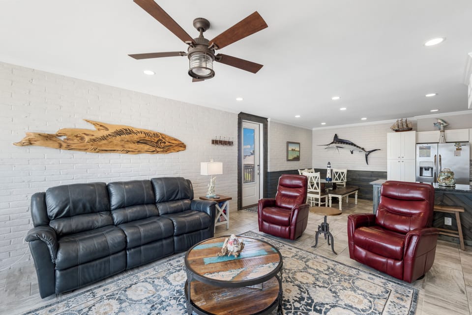 Relax in your nautical-themed living room with leather seating, coastal artwork, and a ceiling fan keeping you cool.