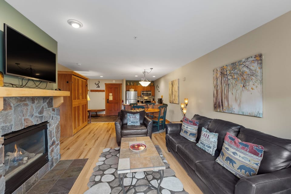 Your cozy mountain retreat features rich leather seating, a warm stone fireplace, and open kitchen - perfect for relaxing after outdoor adventures.