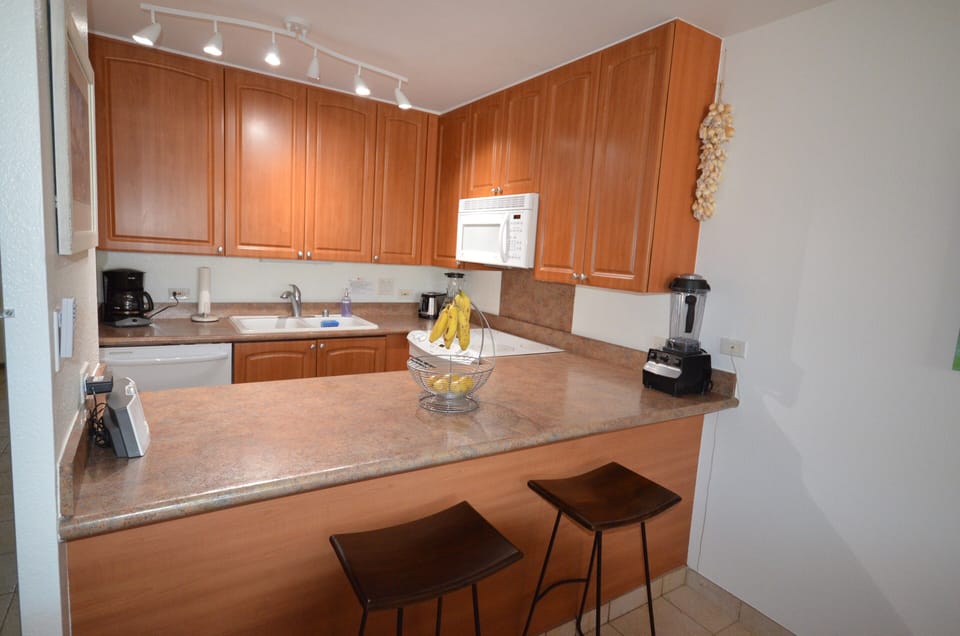 Your fully equipped kitchen awaits with rich wood cabinetry, modern appliances, and a breakfast bar—perfect for preparing tropical meals and enjoying morning coffee together.