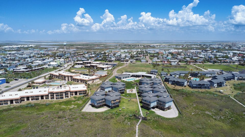 Aerial view of modern vacation rental buildings surrounded by a sprawling coastal community under bright blue skies.