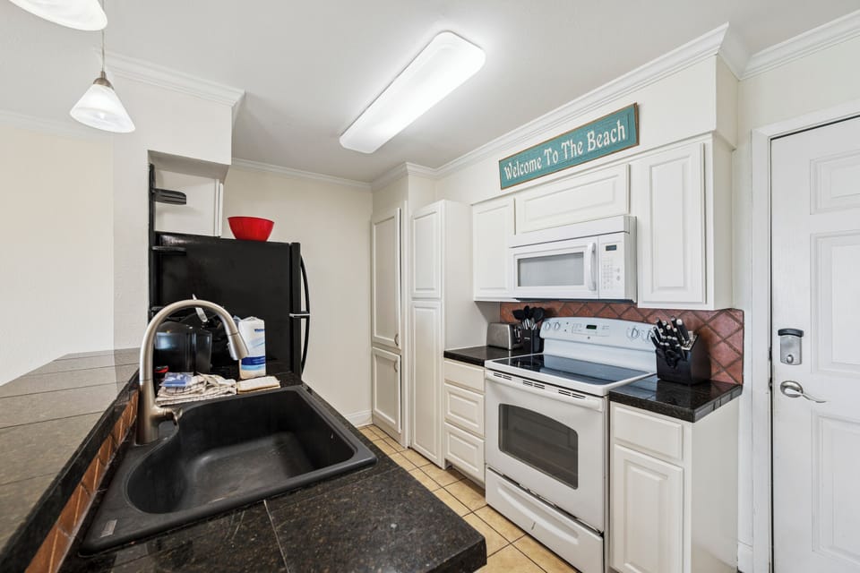 Step into your fully equipped kitchen, complete with modern appliances and beach vibes. Dark granite counters, white cabinetry, and everything you need to whip up your favorite meals. Notice that welcoming beach sign overhead!