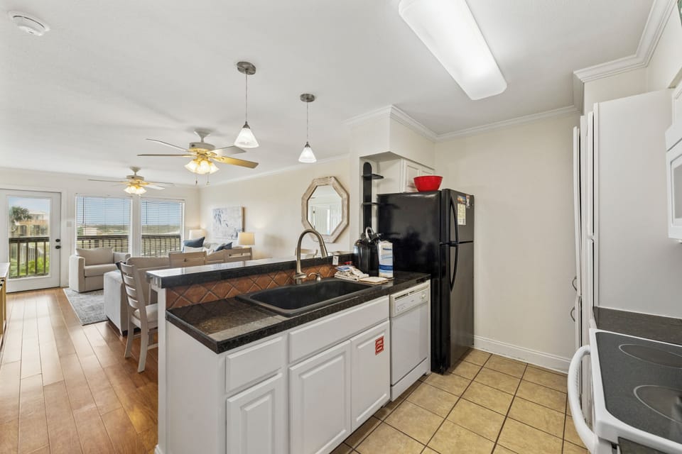 Your fully equipped kitchen flows seamlessly into the bright living area, perfect for preparing meals while staying connected with family. White cabinets, dark countertops, and modern appliances give you everything needed for a comfortable stay.