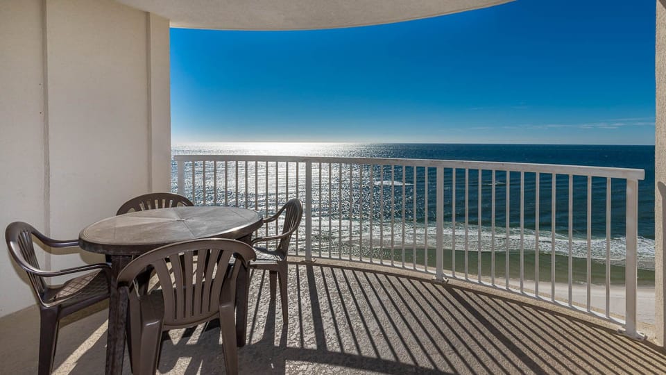 Enjoy a relaxing meal on the balcony with a stunning beach view, featuring a round table and comfortable chairs