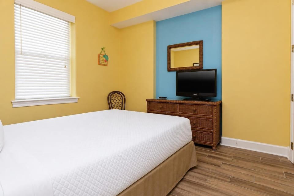 The guest bedroom features cheerful yellow walls, a TV for entertainment, and a comfortable bed for a restful stay