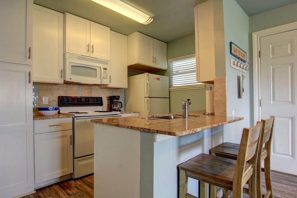 Cook your favorite meals in this bright, fully-equipped kitchen featuring granite countertops, white appliances, and a breakfast bar.