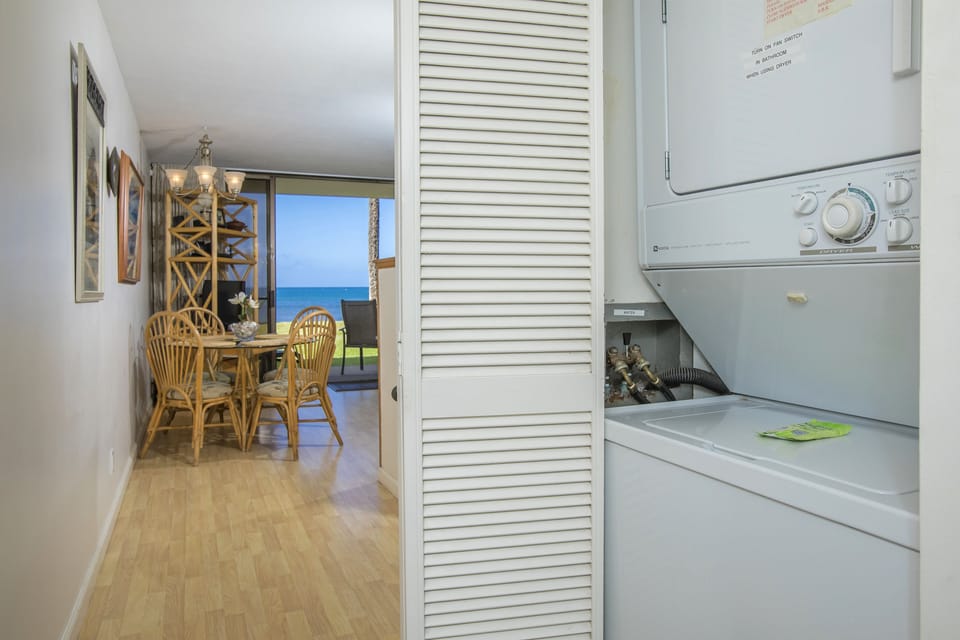 Your vacation home features convenient in-unit laundry facilities, tucked neatly into a hallway closet, with ocean views beckoning from the dining area just beyond.