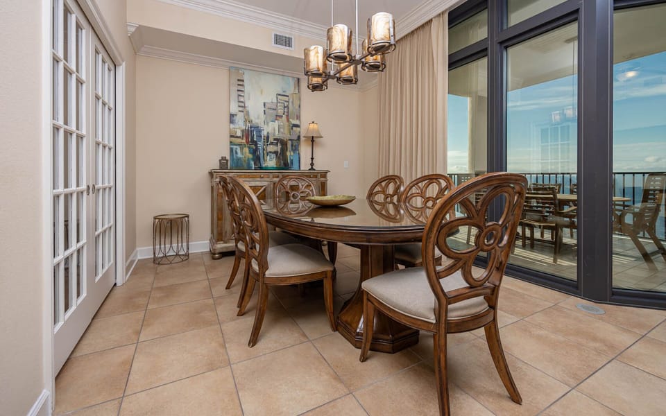 This dining area features elegant wooden table and chairs with a beautiful beach view visible through balcony doors