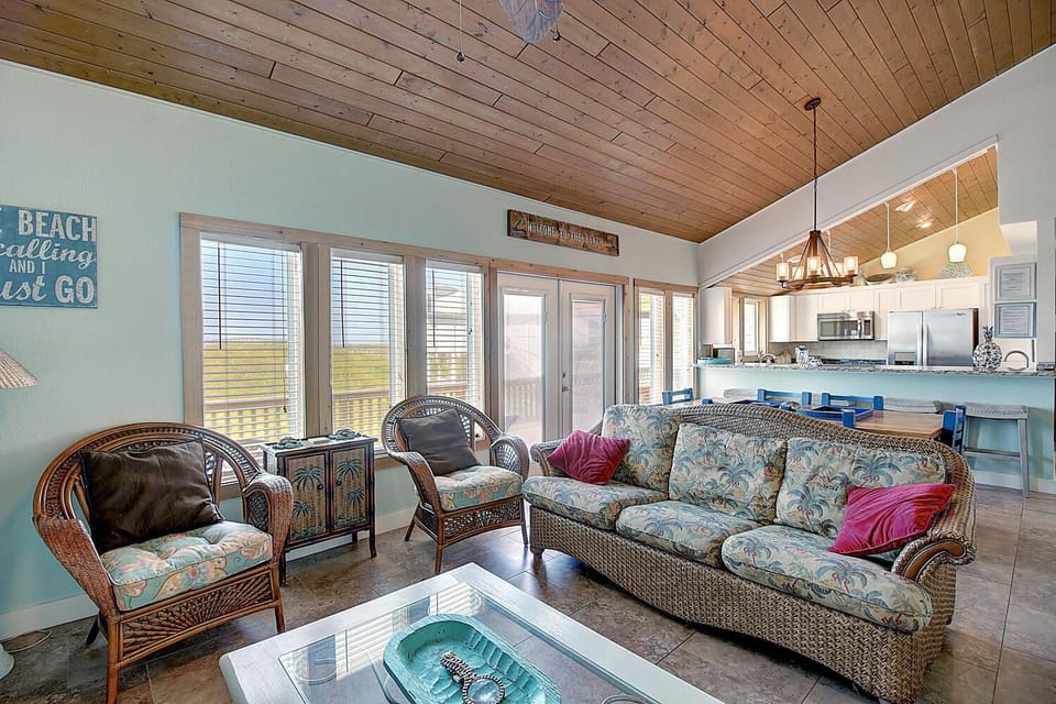 Relax in coastal-style living room with wicker furniture and panoramic windows showcasing beautiful ocean views.