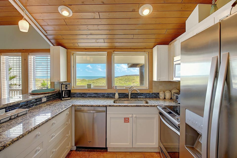 Your fully-equipped kitchen features granite counters and stainless appliances, with stunning ocean views through expansive windows that frame the horizon beautifully.