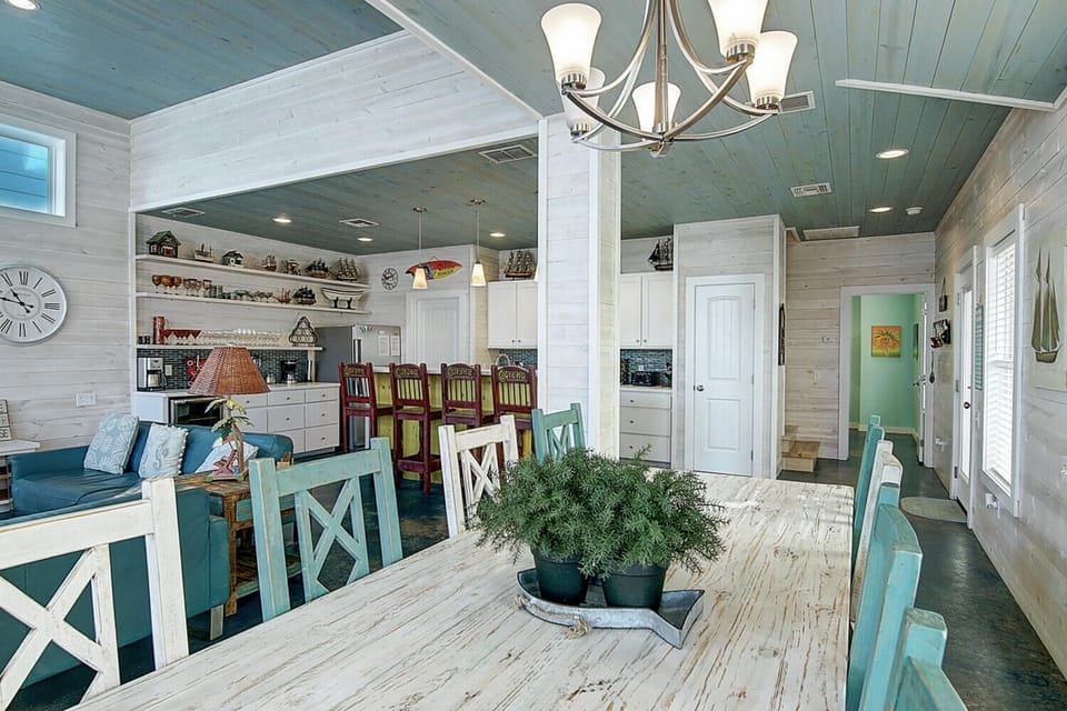 Gather around your rustic farmhouse table beneath coastal-blue ceilings where warm chandeliers cast gentle light over shared meals and memories.