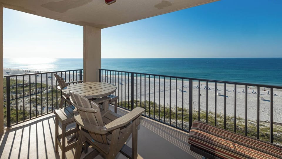 A spacious balcony features a round table and chairs, offering a serene view of the beach and calm blue waters
