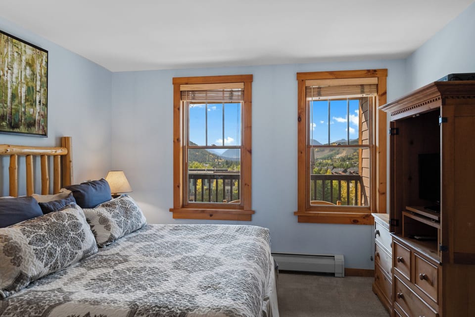 Wake up to stunning mountain views from your cozy bedroom, where warm wood accents and soft blue tones create the perfect alpine retreat.