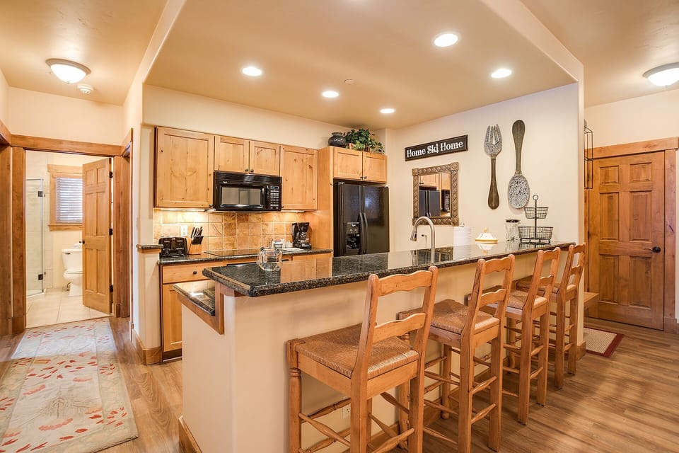 Your fully equipped kitchen invites family gatherings around the spacious granite island, with warm wood accents creating a cozy mountain retreat atmosphere.