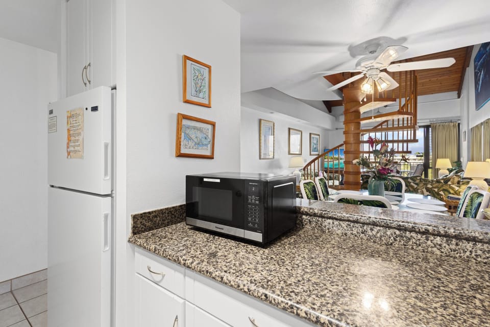 Your modern kitchen features granite countertops, a microwave, and a full-size refrigerator, with an airy open layout leading to the living area and spiral staircase.