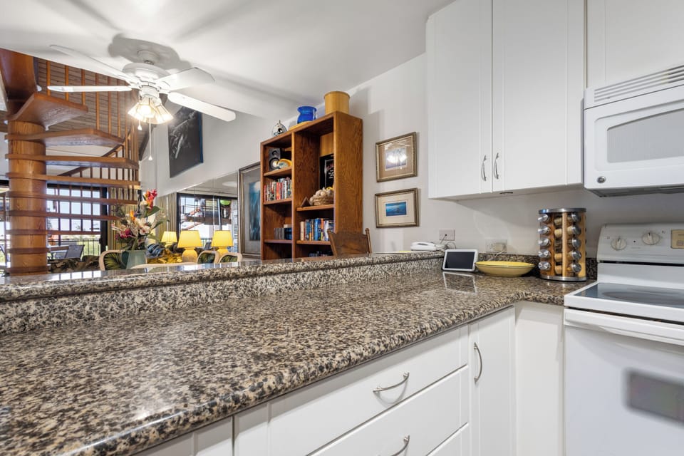 From your kitchen's granite counters, glimpse the cozy living space beyond. Cook, relax, and enjoy the airy, open layout where spiral stairs and warm wood accents invite exploration.