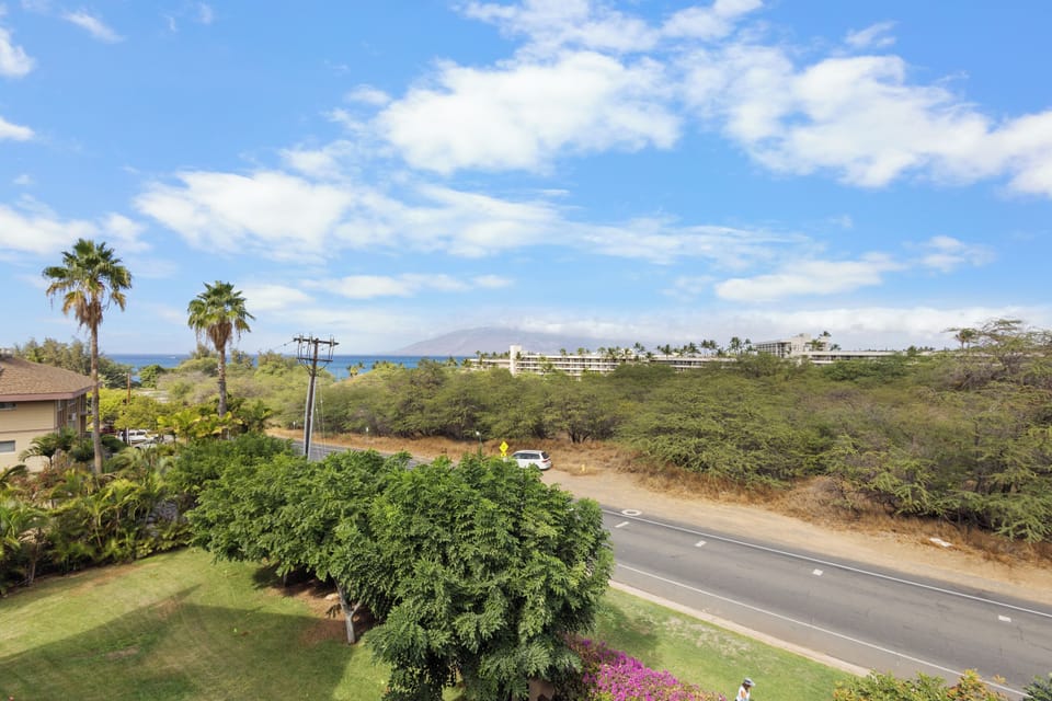 Property overlooks lush tropical greenery with ocean views and neighboring resorts visible in the distance, set in a peaceful Hawaiian neighborhood.