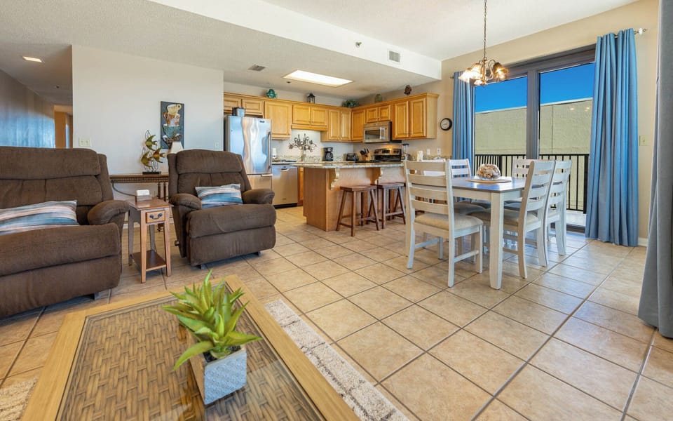 The inviting living area features plush recliners, a dining table, and a fully-equipped kitchen with a breakfast bar