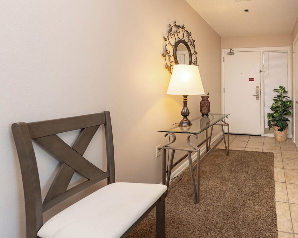 A welcoming entryway features a stylish console table, a decorative lamp, and a comfortable chair beside a potted plant