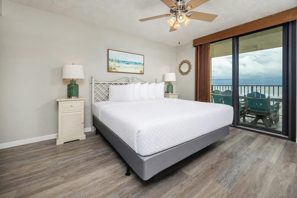 Master bedroom featuring a king bed, coastal artwork, and sliding glass doors leading to a balcony with beach front views