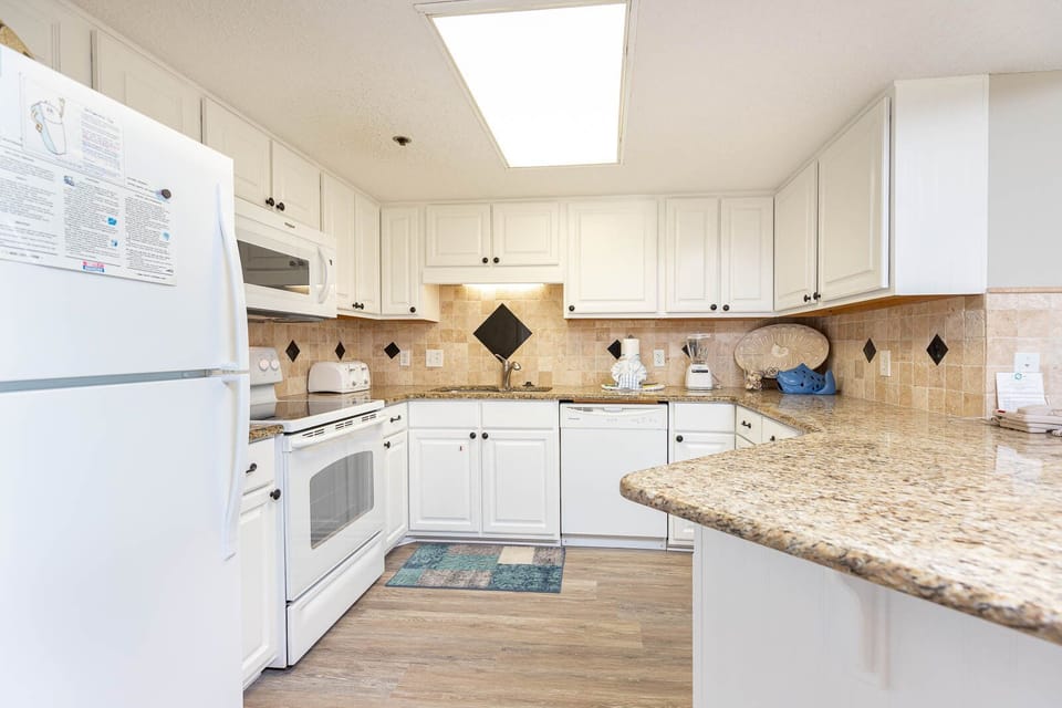 White cabinetry complements the granite countertops in this fully-equipped kitchen, featuring a convenient breakfast bar