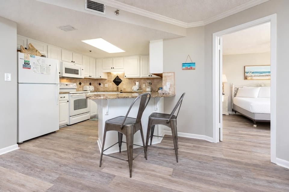 Kitchen area featuring white cabinetry, a granite breakfast bar with metal stools, and a view into the adjacent bedroom
