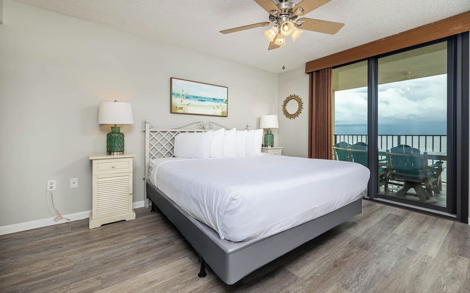 Master bedroom featuring a king bed, coastal artwork, and sliding glass doors leading to a balcony with beach front views