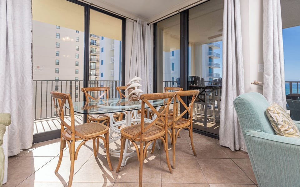 Bright dining area features a glass table surrounded by wooden chairs, with views of the balcony and the beach beyond