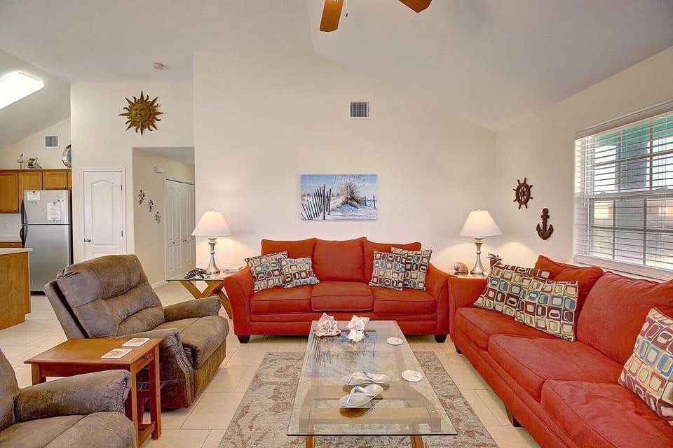 Relax in your bright, open living room with vibrant red sofas, coastal décor, and comfortable seating perfect for unwinding after beach days.