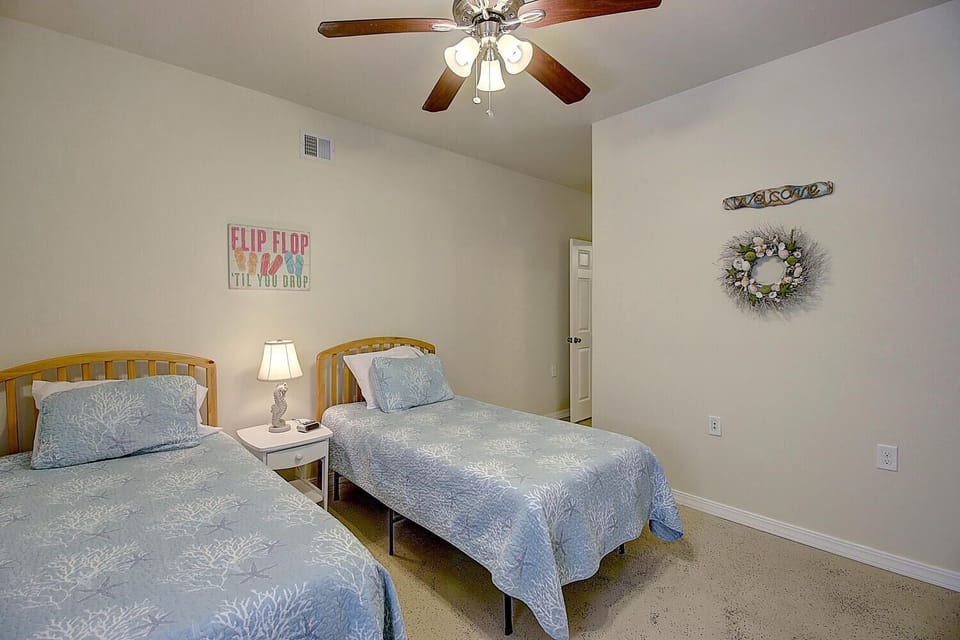 Your peaceful twin bedroom offers comfortable beds with cheerful coastal bedding, ceiling fan for cool nights, and welcoming beach-themed decor.