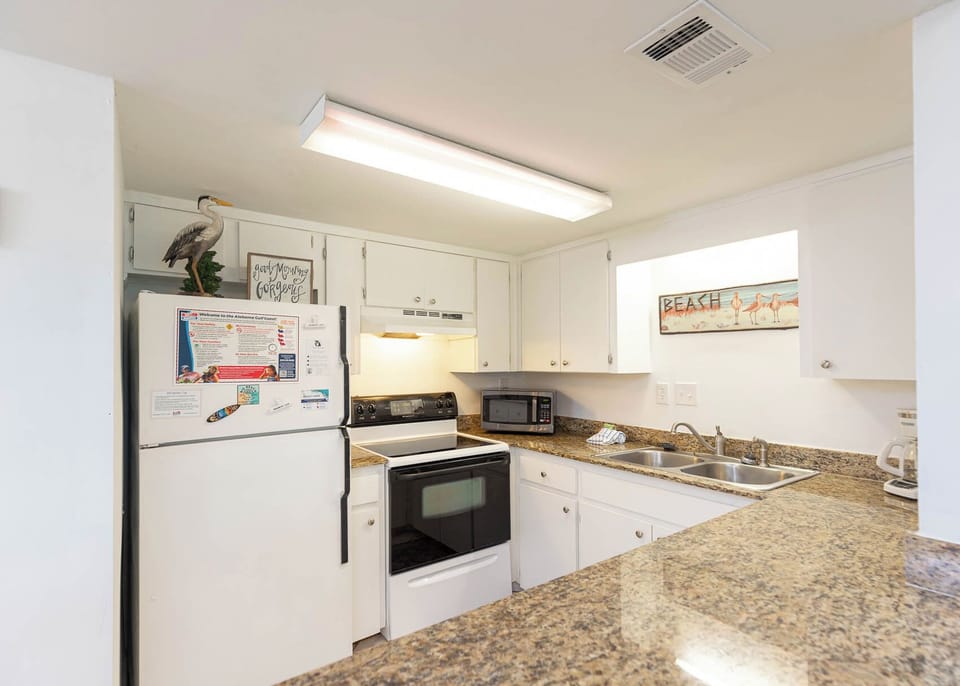 This kitchen features granite countertops, white cabinetry, and a beach-themed decor, perfect for cooking and relaxing