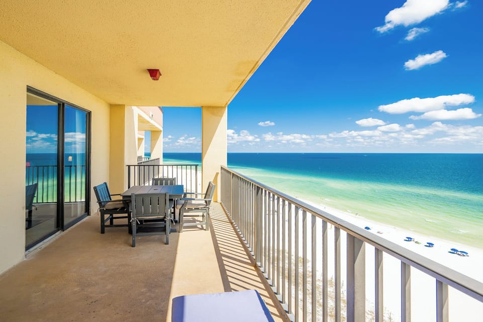 The spacious balcony features a dining table with chairs and offers a breathtaking view of the beach and turquoise waters