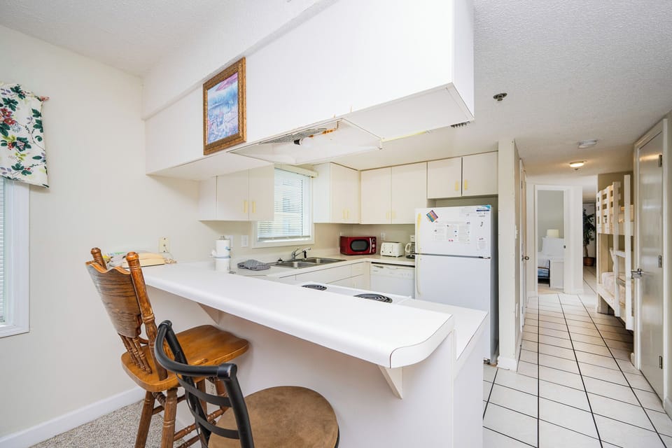 The kitchen features white cabinetry, a cozy breakfast bar, and a glimpse of the hallway leading to additional sleeping areas