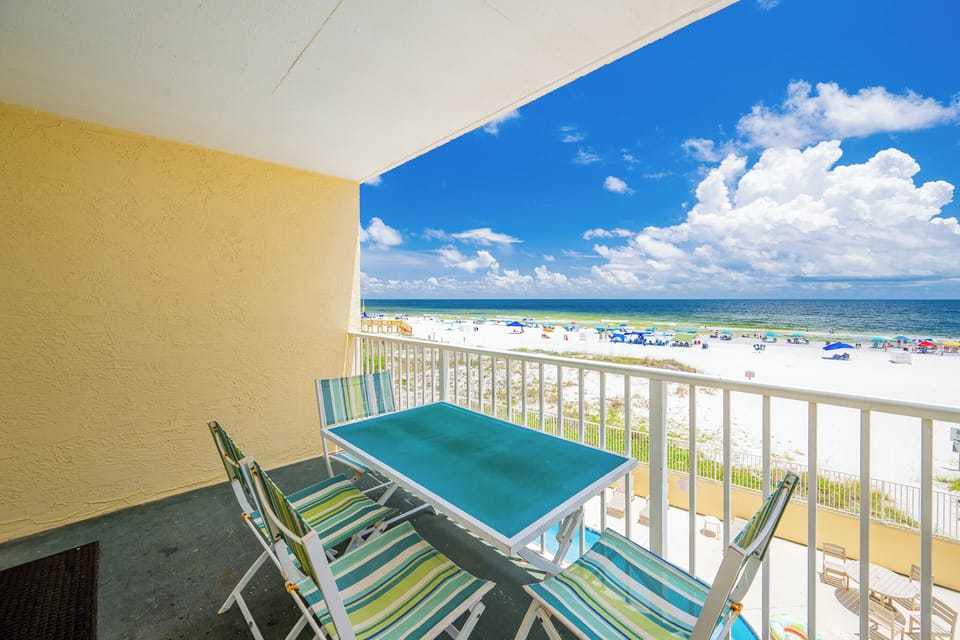 Enjoy a stunning beachfront view from the balcony, featuring a bright turquoise table and colorful striped chairs