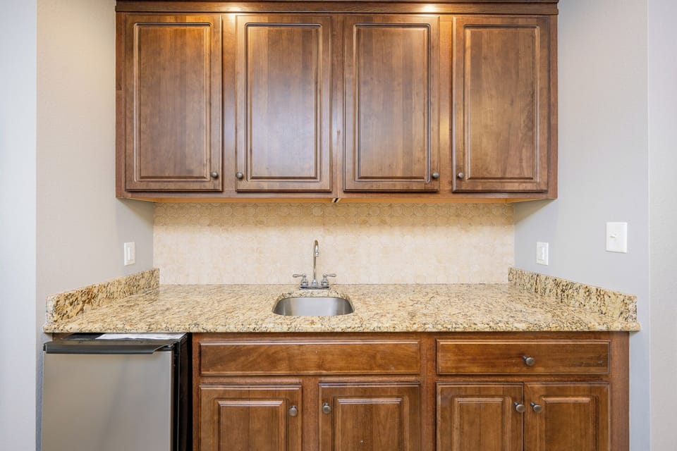 Charming wet bar featuring rich wood cabinetry, and granite countertops, perfect for entertaining guests or a night in