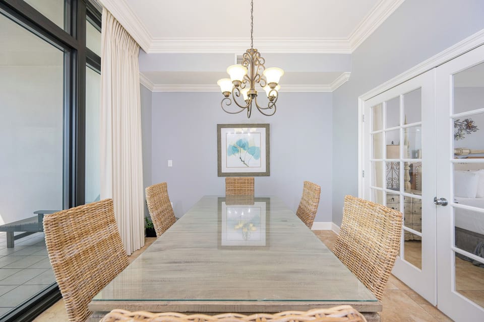 Radiant dining area featuring a glass table and woven chairs, with elegant lighting and a serene coastal-inspired decor