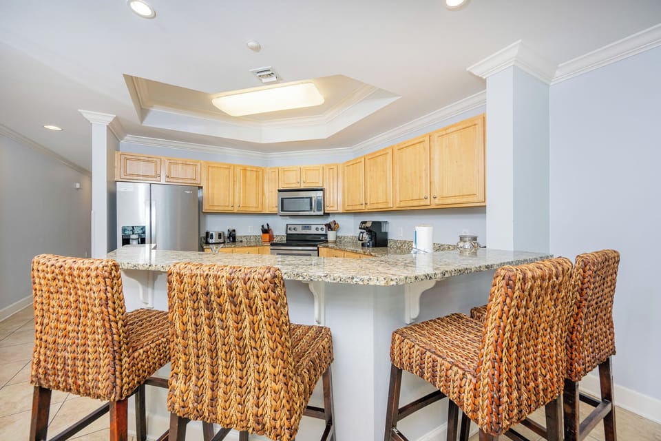 Bright kitchen with granite countertops, stainless appliances, and stylish woven barstools for casual dining